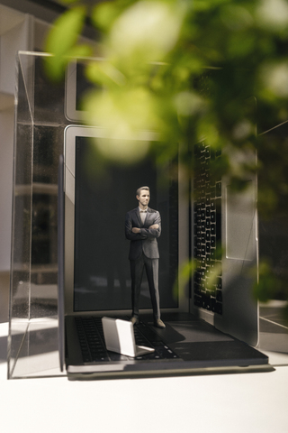 Businessman figurine standing on portable devices under a green plant stock photo