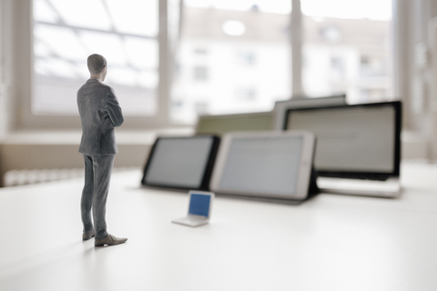 Businessman figurine standing on desk, facing mobile devices stock photo