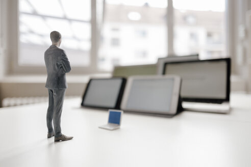 Businessman figurine standing on desk, facing mobile devices - FLAF00038