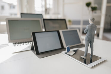 Businessman figurine standing on desk, facing mobile devices - FLAF00039