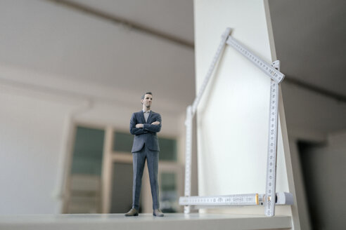 Businessman figurine standing on table with pocket rule, shaping a house - FLAF00057