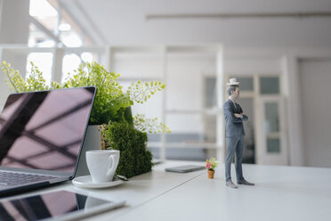 Businessman figurine standing on desk, balancing a cup of coffee on top of his head - FLAF00058