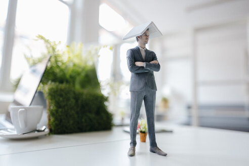 Businessman figurine standing on desk, balancing a laptop on top of his head - FLAF00059