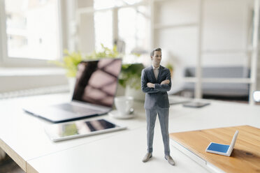 Businessman figurine standing on a desk with mobile devices - FLAF00062