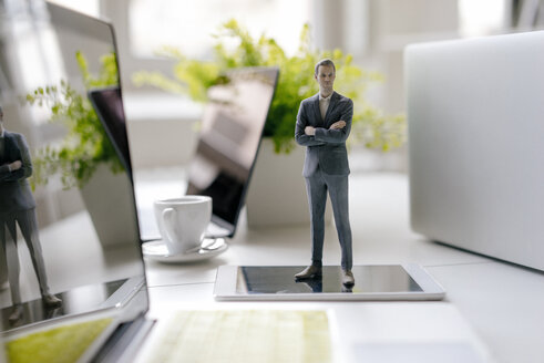 Businessman figurine standing on a desk with mobile devices and a cup of coffee - FLAF00067