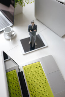 Businessman figurine standing on a desk with mobile devices and a cup of coffee - FLAF00068