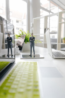 Businessman figurine standing on a desk with mobile devices - FLAF00069