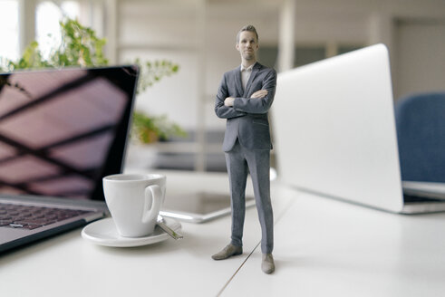 Businessman figurine standing on a desk with mobile devices and a cup of coffee - FLAF00070