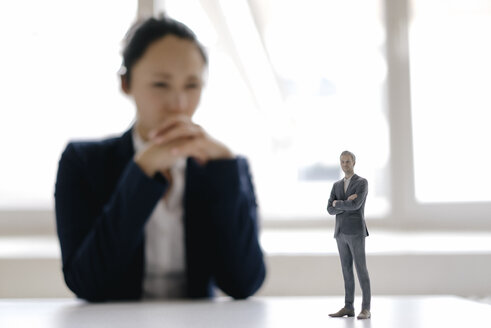 Businesswoman watching businessman figurine, standing on her desk - FLAF00077