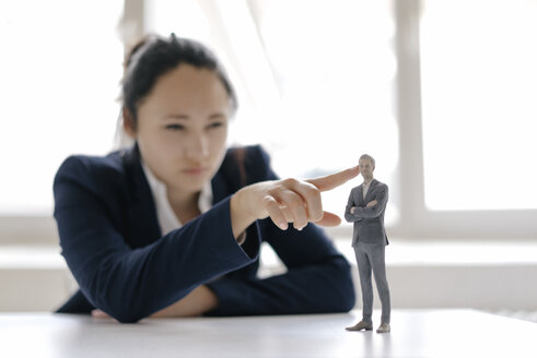 Businesswoman watching businessman figurine, standing on her desk - FLAF00078