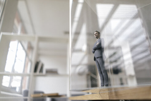 Businessman figurine standing in modern office, looking through glass pane - FLAF00079