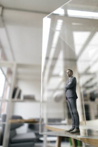 Geschäftsmann in einem modernen Büro stehend, durch eine Glasscheibe blickend, lizenzfreies Stockfoto