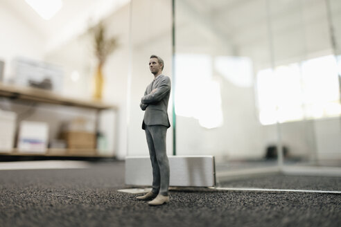 Businessman figurine standing in front of glass wall in office - FLAF00084
