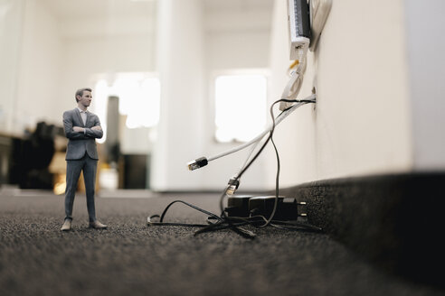 Businessman figurine standing in office, looking at disconnected cables - FLAF00096