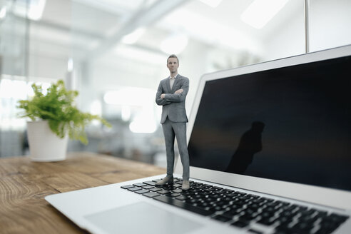 Businessman figurine standing on laptop in modern office - FLAF00099