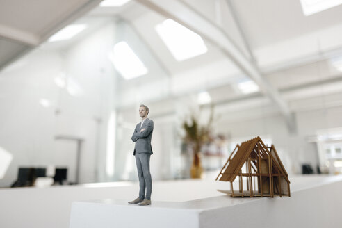 Businessman figurine standing on desk next to architectural model - FLAF00100