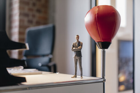 Businessman figurine standing on desk by punching ball - FLAF00105