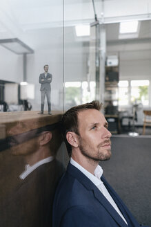 Geschäftsmann sitzt in seinem Büro mit seinem 3D-Porträt hinter einer Glasscheibe - FLAF00108