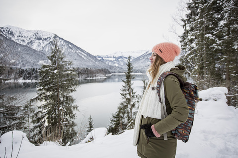 Junge Frau steht in alpiner Winterlandschaft mit See, lizenzfreies Stockfoto