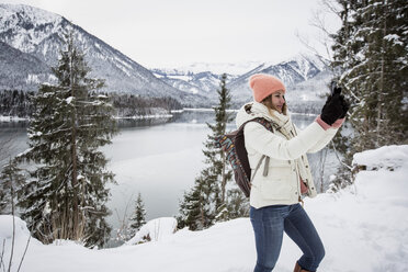 Young woman taking a selfie in alpine winter landscape with lake - SUF00405