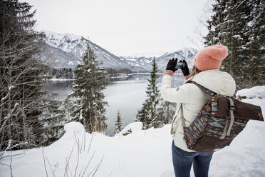 Junge Frau beim Fotografieren in alpiner Winterlandschaft mit See - SUF00406