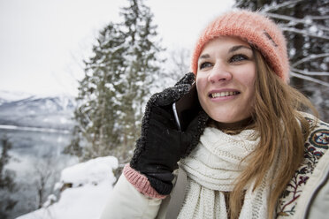 Porträt einer lächelnden jungen Frau am Handy in alpiner Winterlandschaft - SUF00409