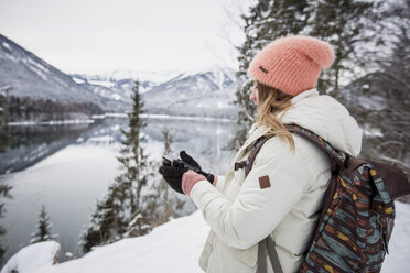 Junge Frau mit Mobiltelefon in alpiner Winterlandschaft mit See - SUF00411