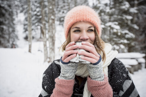 Porträt einer jungen Frau, die im Winter im Freien ein heißes Getränk trinkt - SUF00415