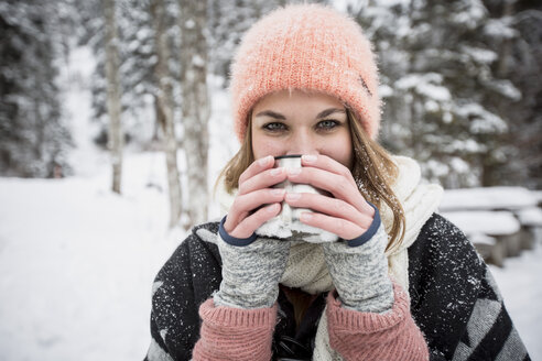 Porträt einer jungen Frau, die im Winter im Freien ein heißes Getränk trinkt - SUF00416