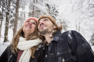 Smiling couple in winter forest watching snow fall - SUF00436