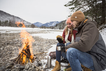 Couple on a trip in winter having a break at camp fire - SUF00445