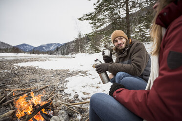 Couple on a trip in winter having a hot drink at camp fire - SUF00446