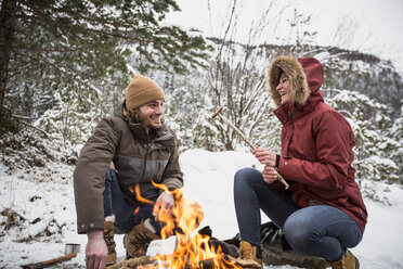 Happy couple on a trip in winter having a break at camp fire - SUF00447