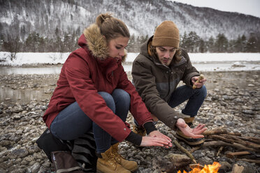 Couple on a trip in winter warming hands at camp fire - SUF00449