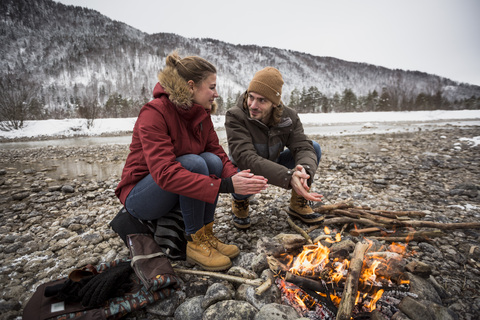 Paar auf einer Reise im Winter wärmt sich die Hände am Lagerfeuer, lizenzfreies Stockfoto