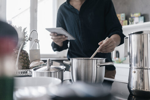 Mann steht in der Küche und liest Nachrichten auf seinem digitalen Tablet, während er kocht - KNSF03424