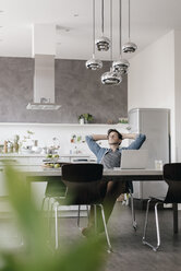 Young man relaxing at table in the kitchen - KNSF03426