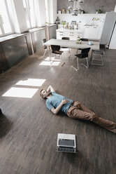 Nachdenklicher Mann auf dem Boden liegend in einem Loft - KNSF03428