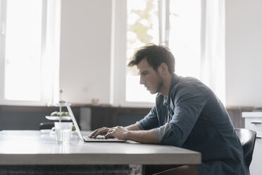 Young man sitting at table working on laptop - KNSF03436