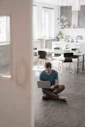 Mann sitzt in der Küche auf dem Boden und arbeitet am Laptop - KNSF03448