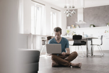 Mann sitzt auf dem Boden in einem Loft und arbeitet an einem Laptop - KNSF03449