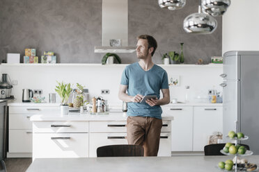 Man with tablet standing in the kitchen looking at distance - KNSF03452