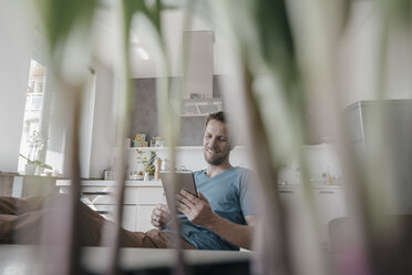 Man sitting at table in the kitchen looking at tablet - KNSF03455