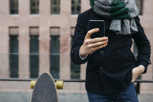 Mann mit Handy und Skateboard in der Stadt, Teilansicht - JRFF01493