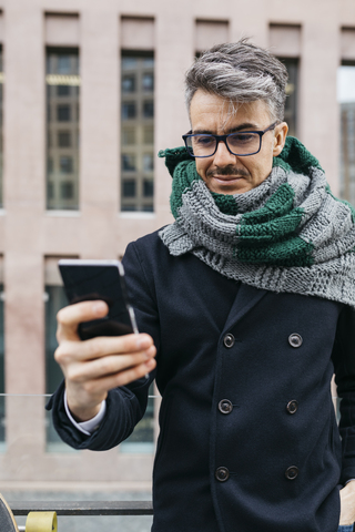 Porträt eines lächelnden Mannes, der in der Stadt auf sein Handy schaut, lizenzfreies Stockfoto