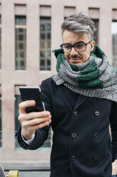 Portrait of smiling man looking at cell phone in the city - JRFF01494