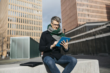 Businessman sitting on bench in the city using tablet - JRFF01496