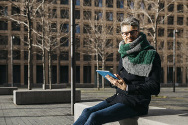 Geschäftsmann mit Tablet sitzt auf Bank in der Stadt im Winter - JRFF01498