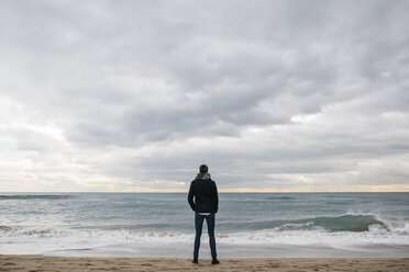 Rückenansicht eines Mannes, der im Winter am Strand steht und in die Ferne schaut - JRFF01506