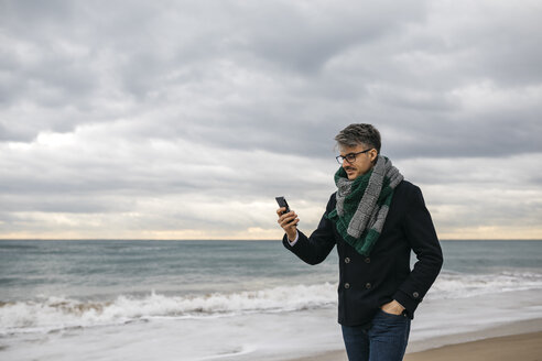 Geschäftsmann am Strand schaut auf sein Handy - JRFF01507